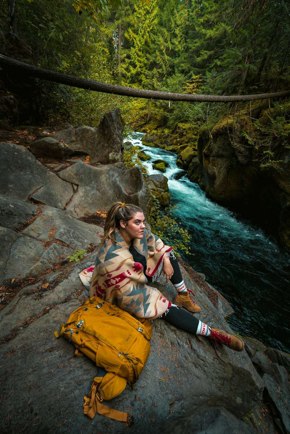 woman in pink jacket sitting on rock near river during daytime