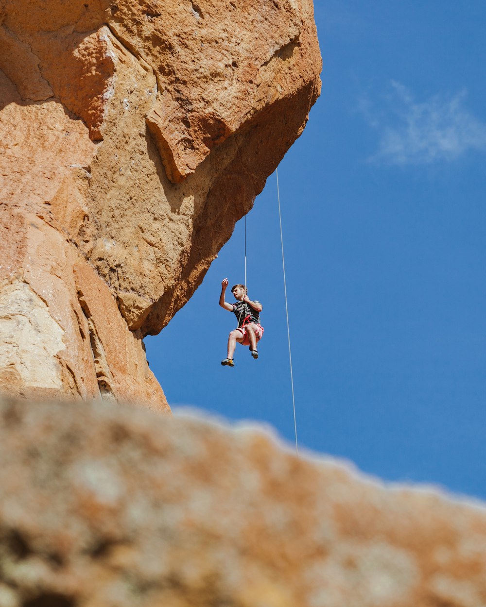 man in black shirt and black shorts jumping on brown rock during daytime