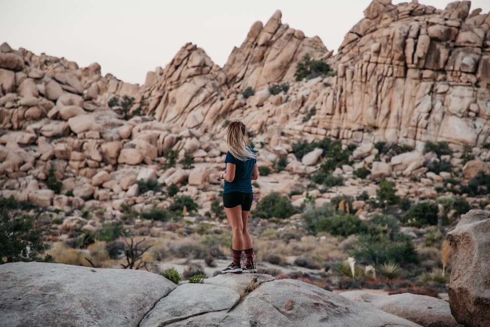 woman in black tank top and black shorts standing on rocky mountain during daytime