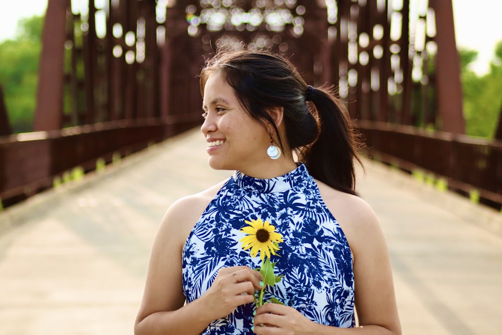 woman in blue and white floral sleeveless dress holding purple flower