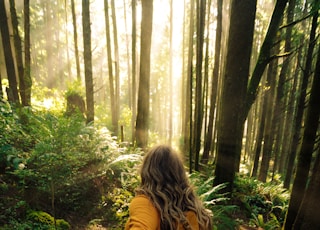 woman in brown jacket standing in forest during daytime