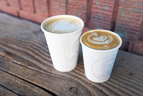 Close-up of coffee cups with latte art on a wooden table.