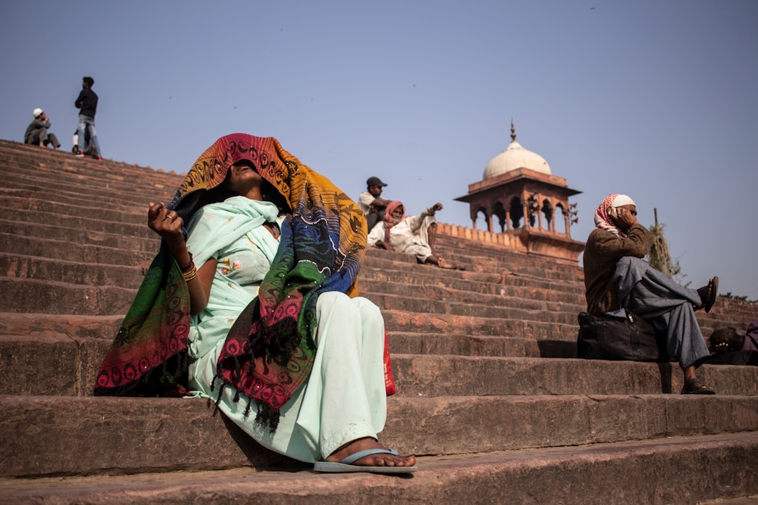 woman in green and red sari sitting on brown concrete stairs during daytime