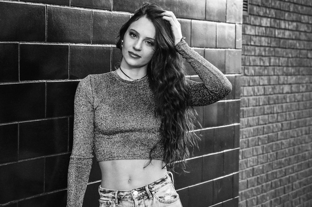 woman in gray sweater standing beside brick wall