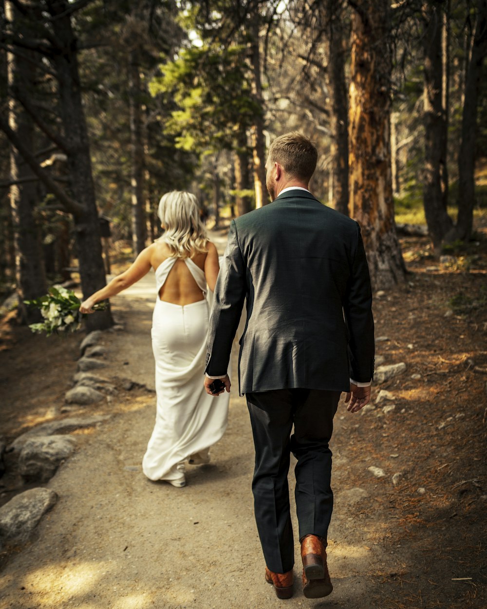 man in black suit jacket and woman in white dress walking on pathway during daytime