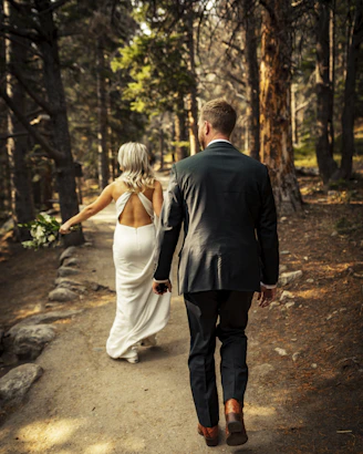 man in black suit jacket and woman in white dress walking on pathway during daytime