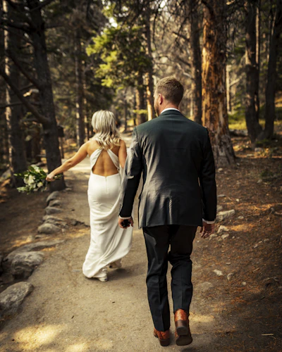 man in black suit jacket and woman in white dress walking on pathway during daytime