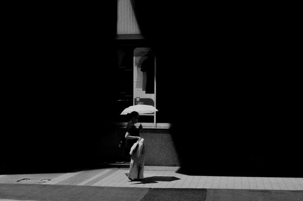 grayscale photo of woman in white dress walking on sidewalk