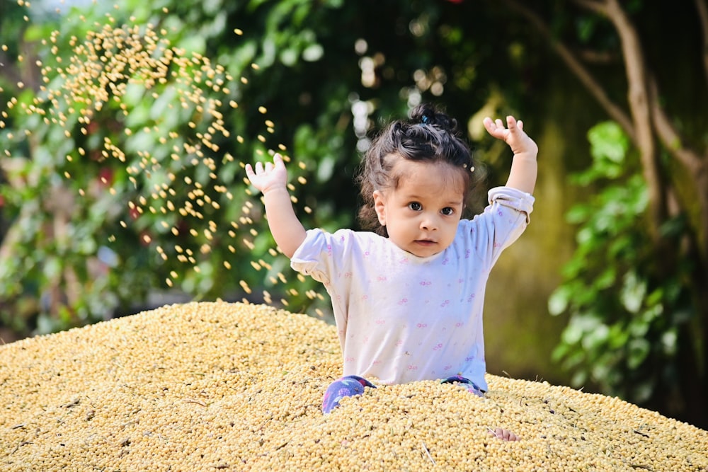 girl in white long sleeve shirt and blue pants sitting on brown dried leaves during daytime