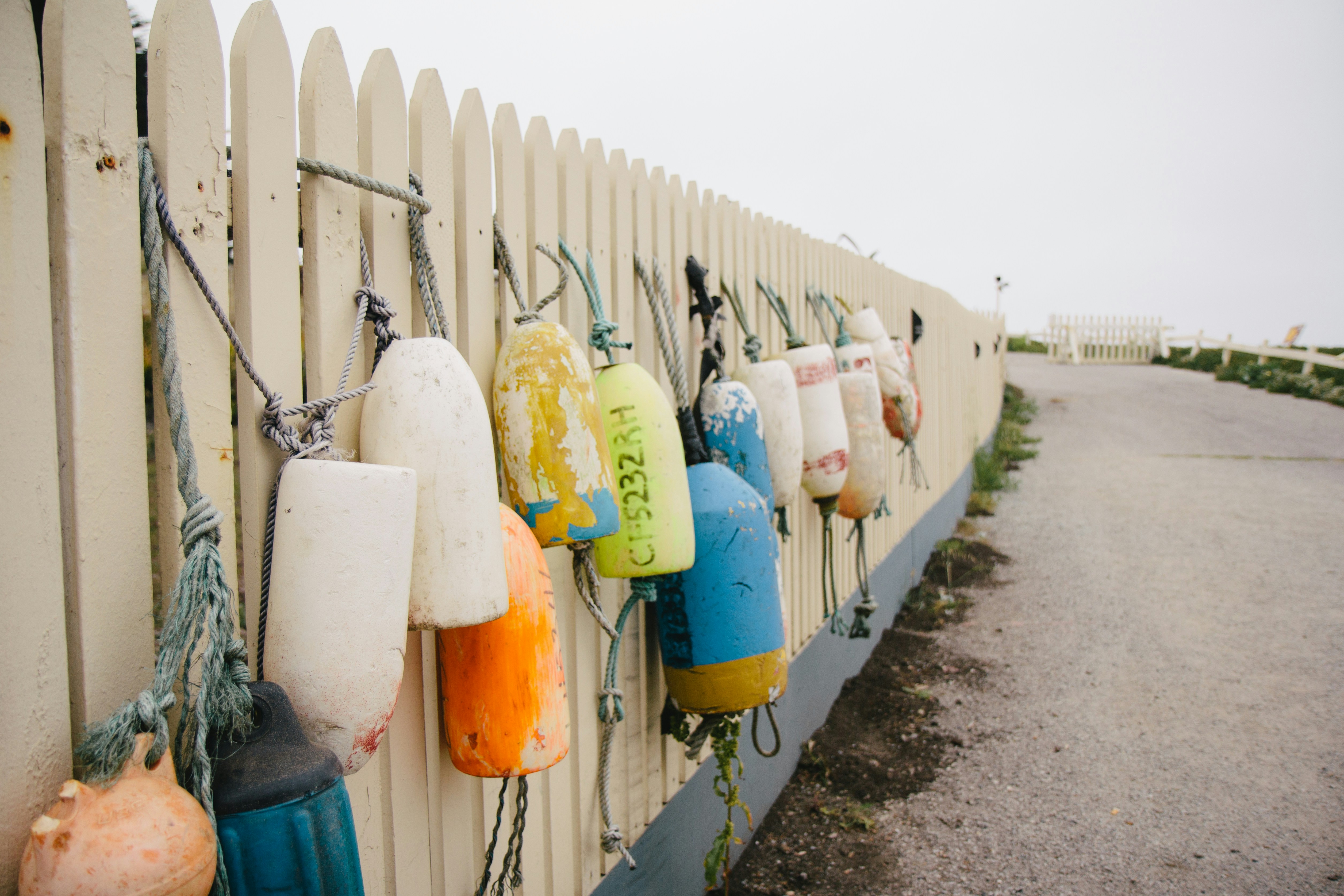 yellow and blue plastic container hanged on white wooden fence during daytime