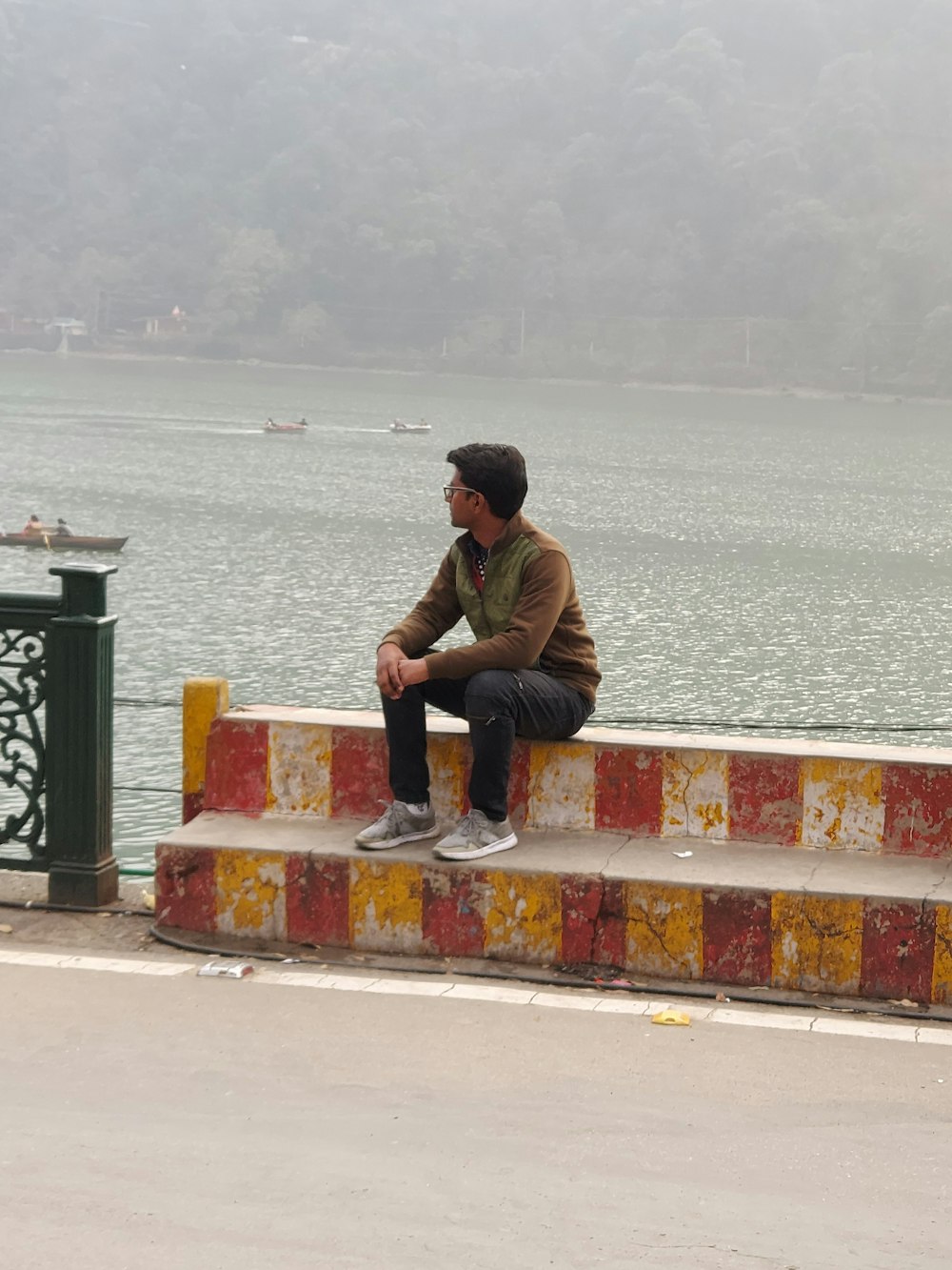 man in brown jacket sitting on concrete bench near body of water during daytime