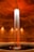 A cylindrical room featuring a central column of water illuminated dramatically from above. The water cascades into a circular pool surrounded by concrete walls. Warm lighting accentuates the reddish-brown tones of the space, adding a serene and mysterious atmosphere.