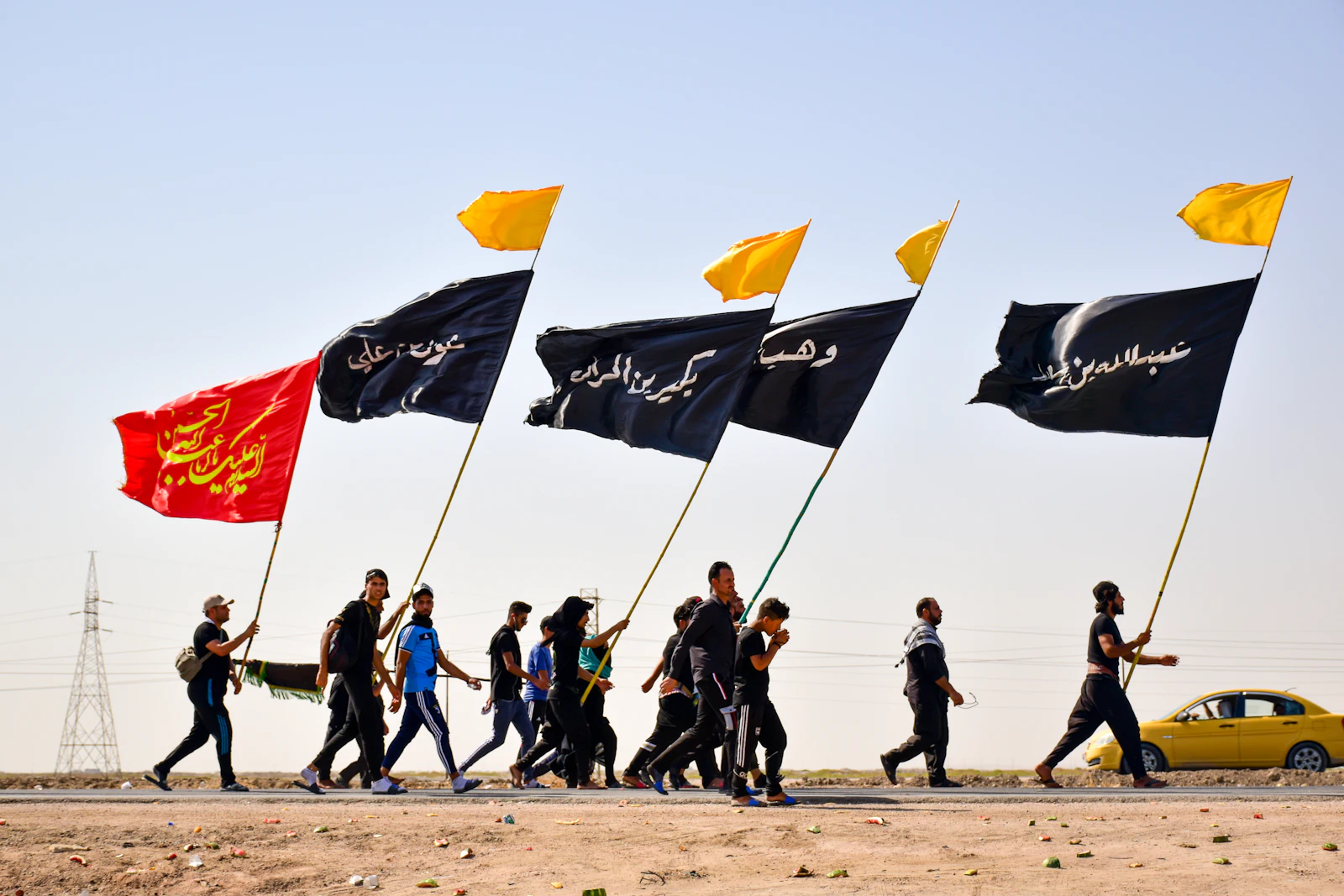 Pilgrims walking the desert road with flags in bright daylight
