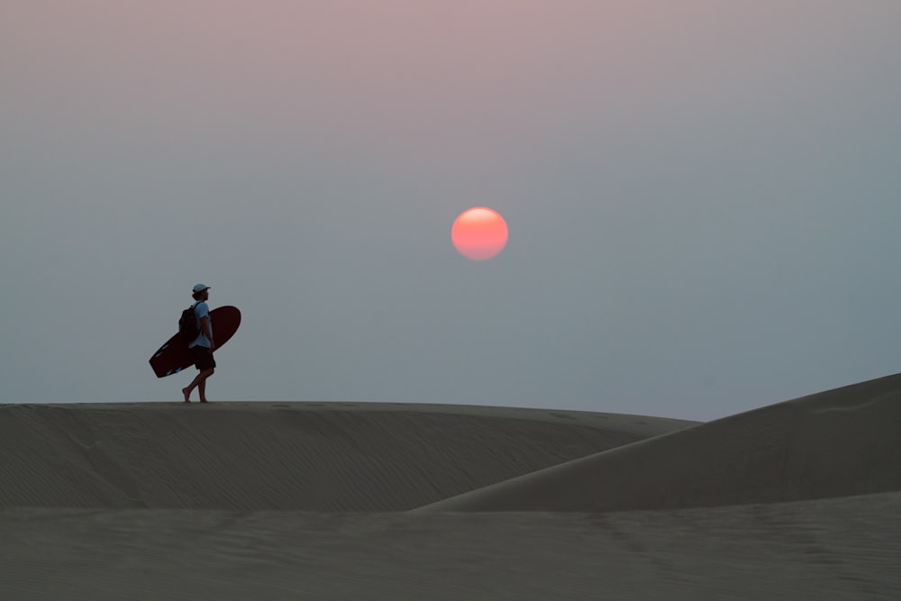 man in black jacket and pants walking on gray sand during sunset