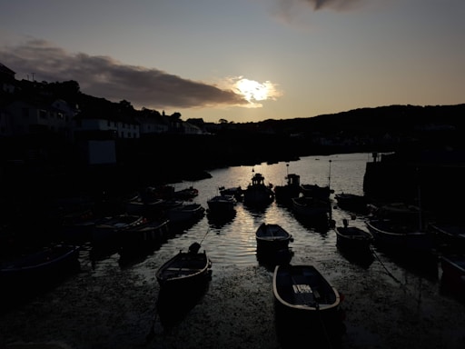 A calm harbor scene at dusk with docked ships and glowing lights reflecting on the water.
