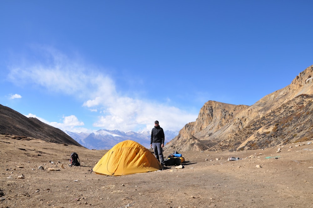 man in black jacket sitting on camping chair near yellow tent during daytime