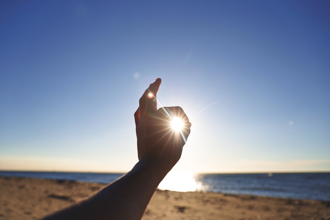 person raising his left hand near sea during daytime