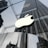 A large, illuminated apple logo suspended in front of a modern glass building. The glass walls reflect the surrounding architecture, including a tall skyscraper and other urban structures, creating a sleek and modern cityscape.