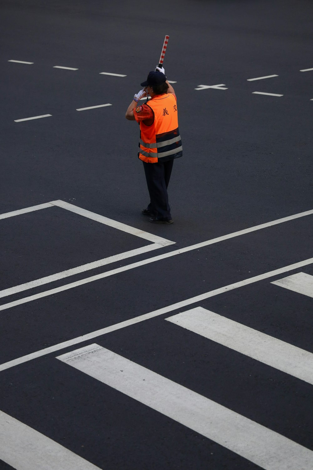 man in orange jacket and black pants standing on black and white pedestrian line