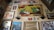 A collage of vintage and retro-style posters and advertisements covers a wall. Various framed artworks depict classic brand logos, drinks, and pin-up art. Notable elements include a large painting featuring bottles and a lime, a retro advertisement with a glamorous woman, and a collection of smaller, nostalgic images.
