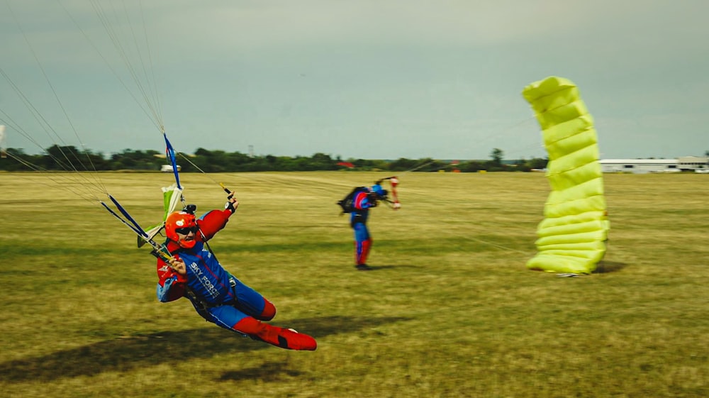 2 men in red and blue shirt and blue pants playing kite surfing during daytime