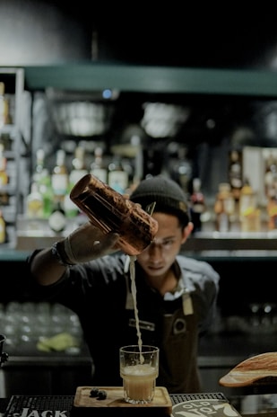 man in black and white polo shirt holding brown glass bottle