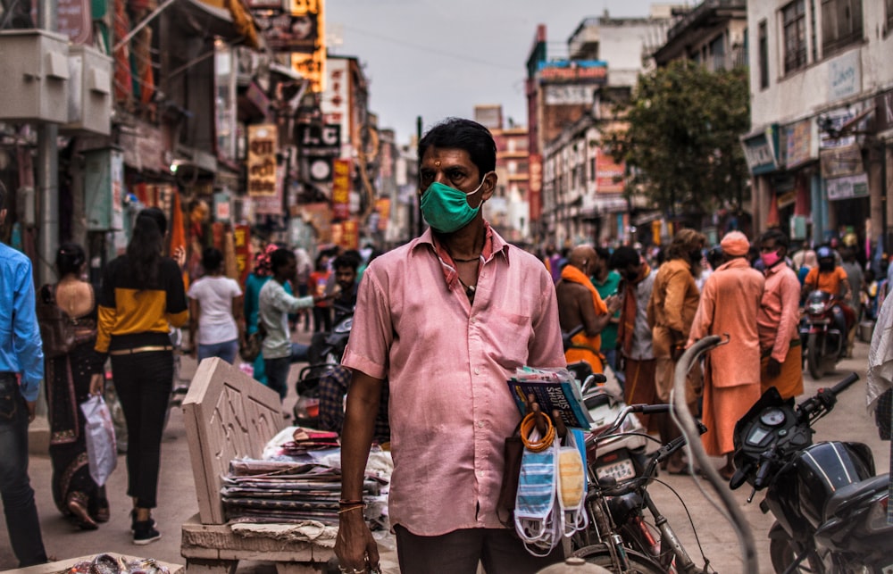 a man wearing a face mask standing in the middle of a crowded street