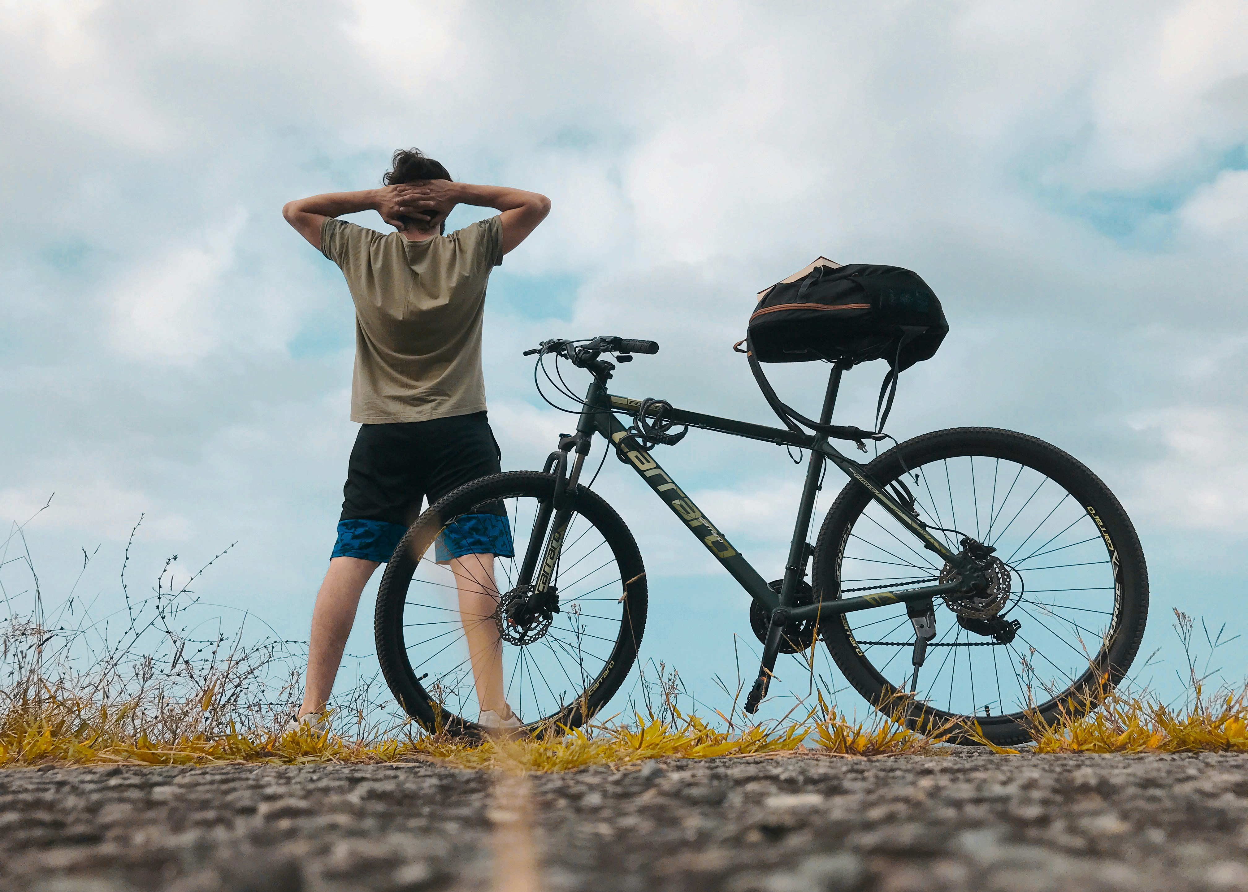 woman in white shirt and blue shorts standing beside black mountain bike