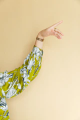 Close-up of a woman's hand wearing thin gold rings and a beige silk sleeve background.