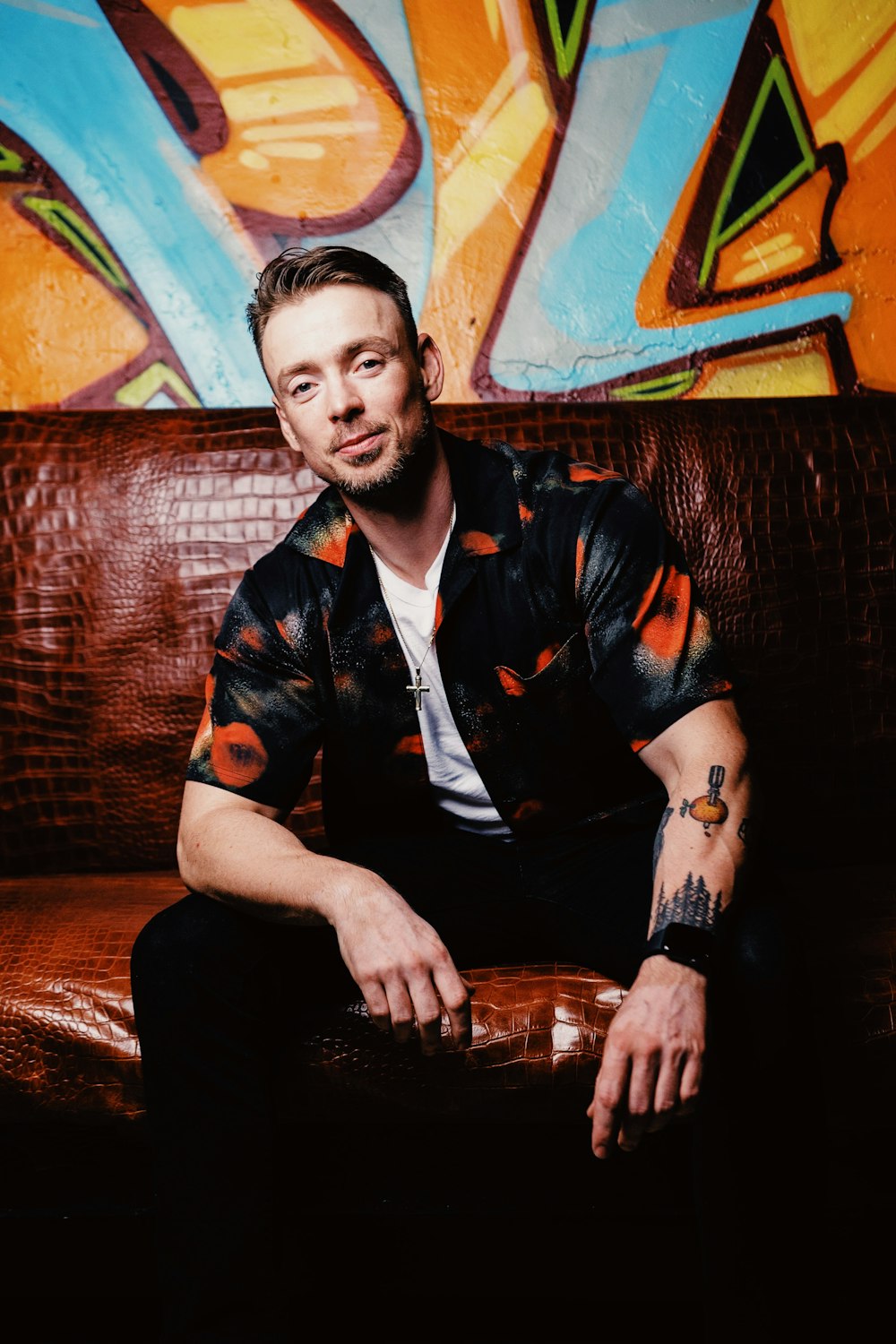 man in black and orange button up shirt sitting on brown sofa