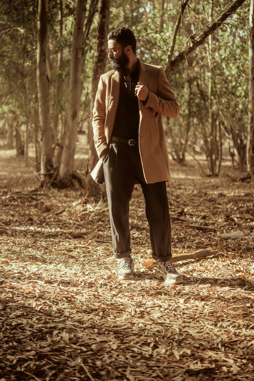 woman in brown coat and black pants standing on brown dried leaves during daytime