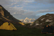 A family setting up a tent on a sunny campground with mountains in the background.