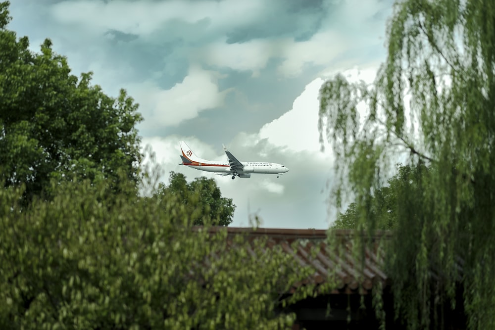 white and red airplane flying over green trees during daytime