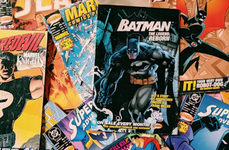A collection of various comic books scattered on a surface. The comic books feature popular superheroes like Batman and Superman. The covers display colorful, dynamic illustrations with bold titles and iconic characters in action poses.