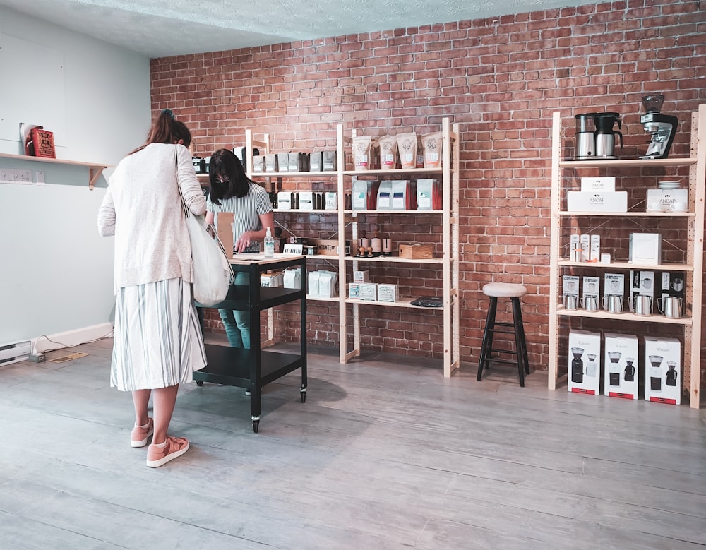 woman in white long sleeve shirt standing beside brown wooden shelf