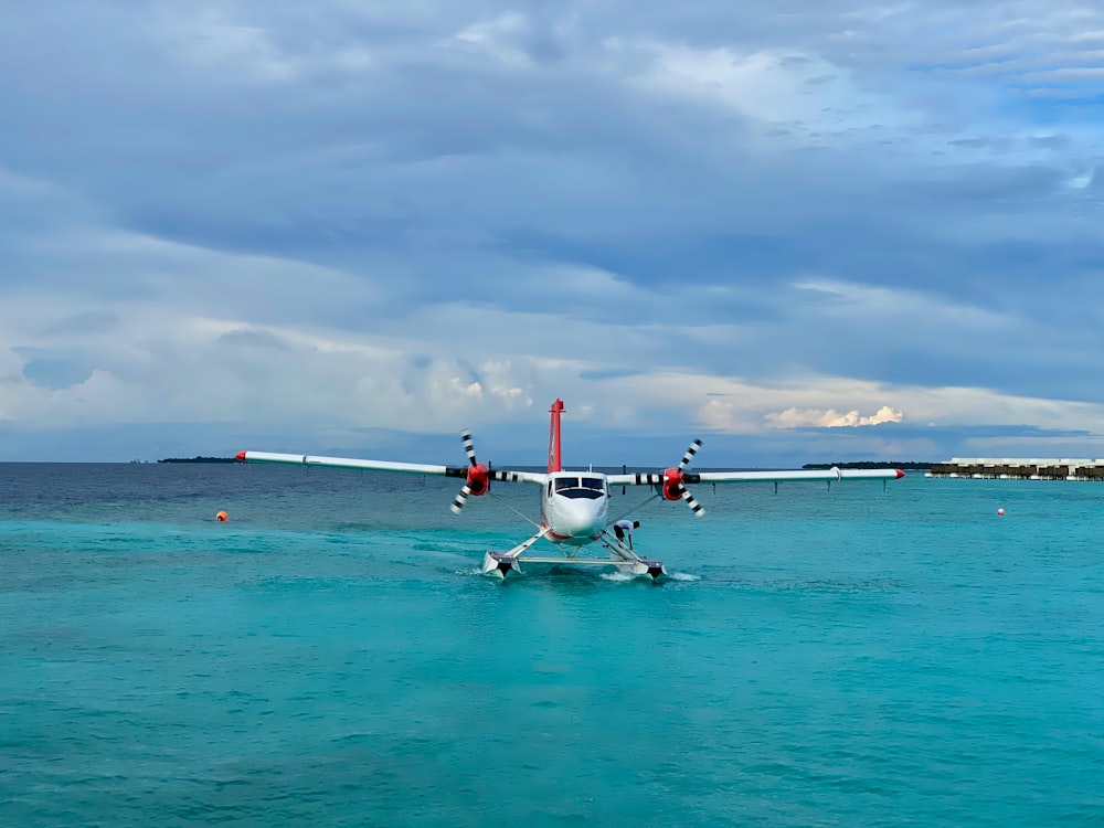 昼間、白い雲の下の海上に浮かぶ白と赤の飛行機