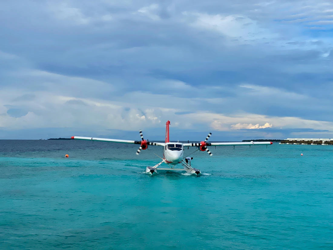 A white and red float plane resting on the open sea under cloud