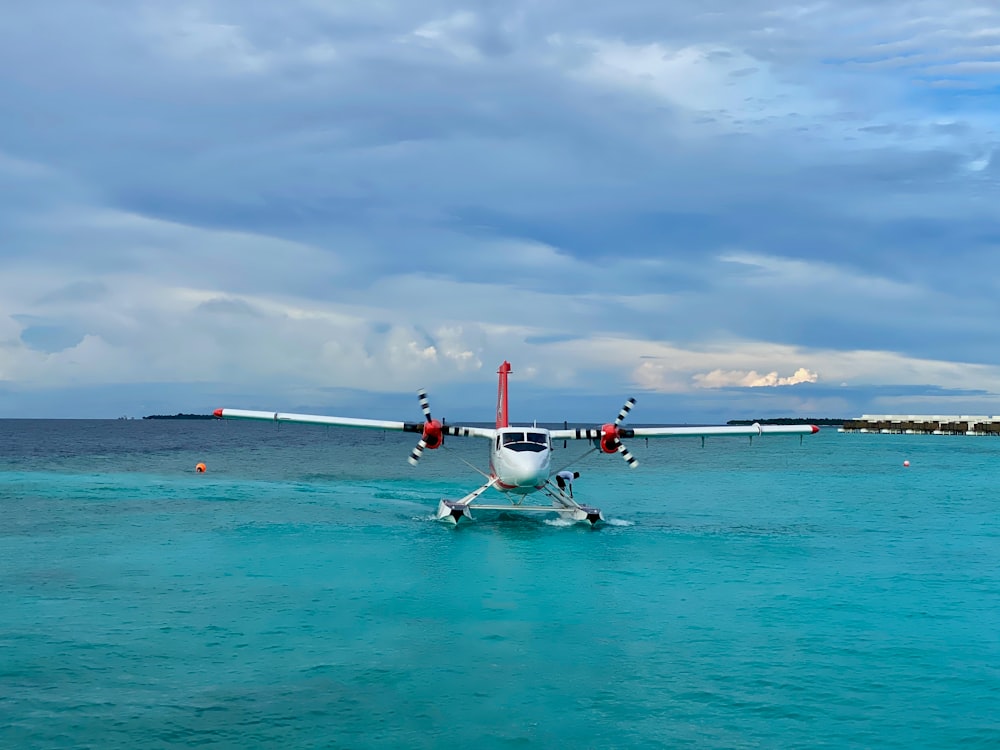 Weißes und rotes Flugzeug tagsüber unter weißen Wolken auf See