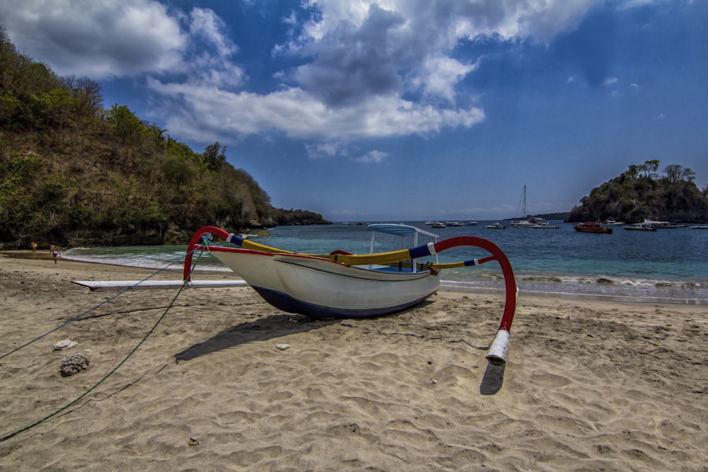 white and red boat on brown sand under blue sky during daytime