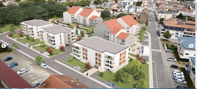 Aerial view of a residential area featuring multiple modern apartment buildings with flat roofs and red-tiled sections. The buildings are surrounded by landscaped greenery, including trees and lawns. Several parked cars line the streets and parking lots. The neighborhood consists of similar architectural styles and is interspersed with roads and pathways.
