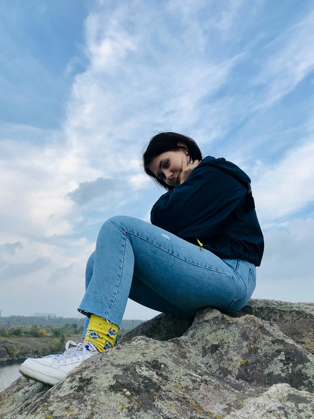 woman in blue hoodie and blue denim jeans sitting on rock during daytime