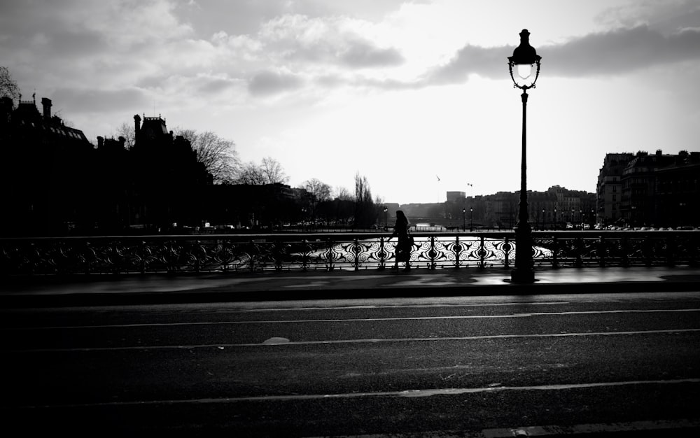 grayscale photo of person standing on bridge