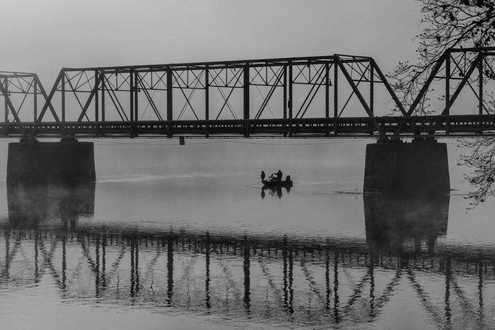 grayscale photo of person riding on horse on river near bridge