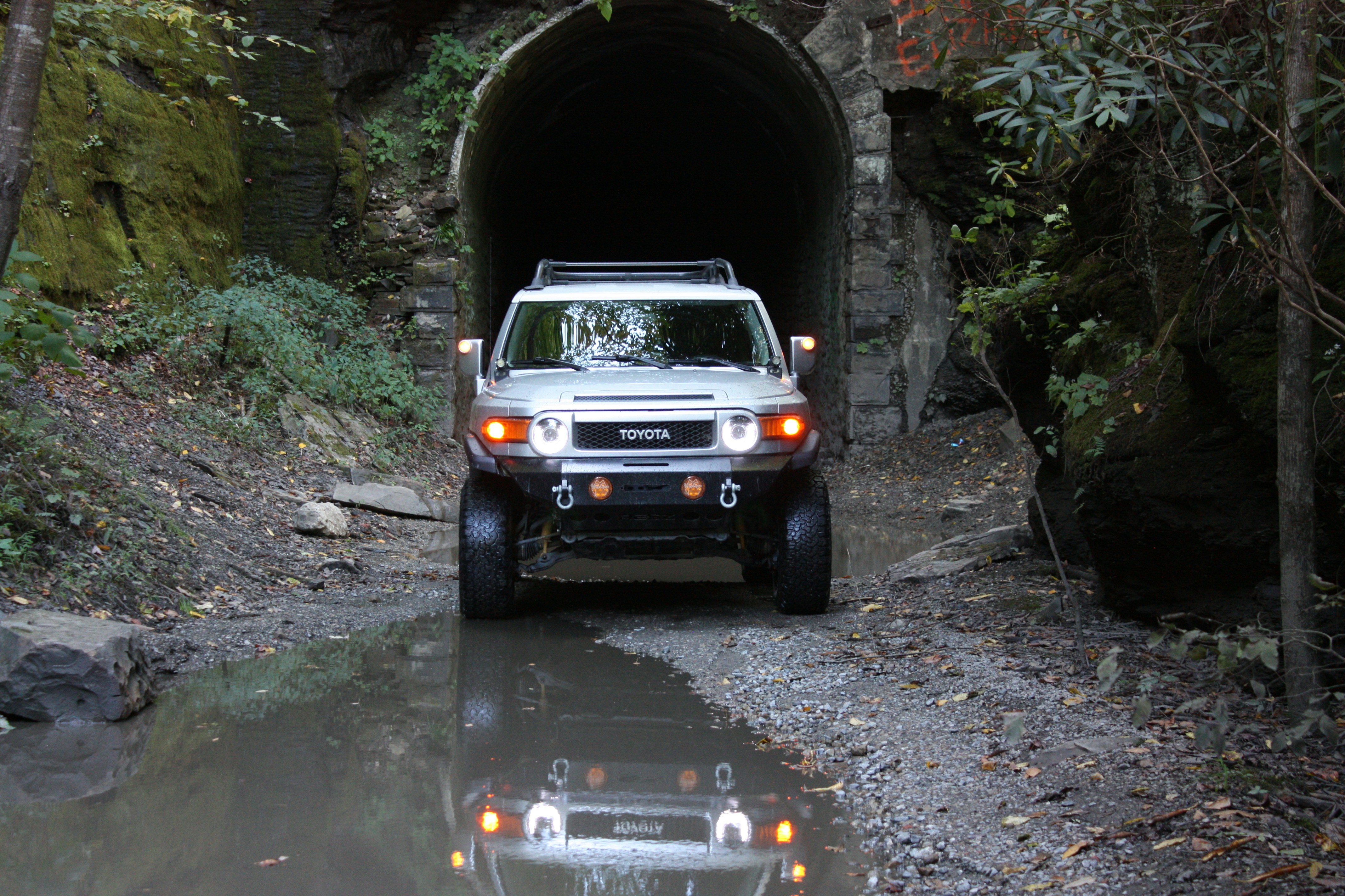 Electric or hybrid off‑road SUV splashing through mud and water on a rugged trail