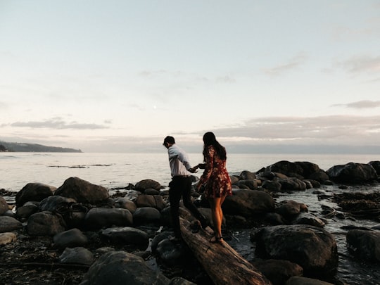 couple standing on rock near body of water during daytime in Sooke Canada