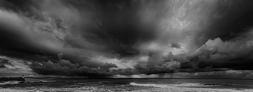 a black and white photo of storm clouds over the ocean