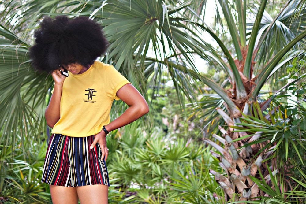 woman in yellow crew neck t-shirt and black and white striped skirt standing near green