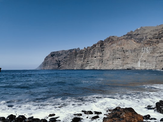 rocky mountain beside body of water during daytime in Playa de los Gigantes Spain