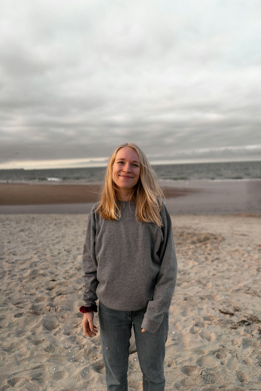 woman in gray sweater standing on brown sand during daytime
