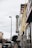 A street view featuring a vintage vertical sign that reads 'Johnson Storage Moving' on the side of a building. The surrounding area includes various storefronts, parked cars along the sidewalk, and a speed limit sign indicating 30 mph. A painted teddy bear mural can be seen near the top of one building, and the sky is overcast, adding a muted tone to the scene.